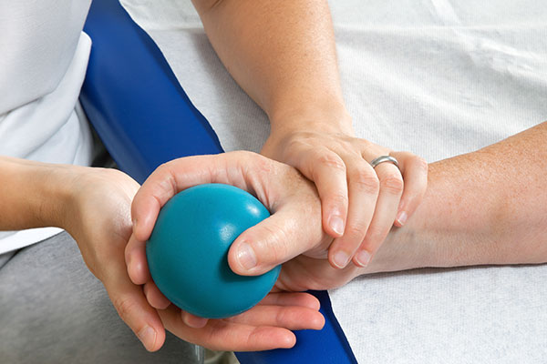 therapist assisting patient holding a ball during hand therapy