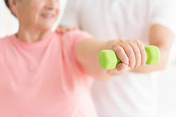 doctor assisting woman holding a green hand weight during therapy