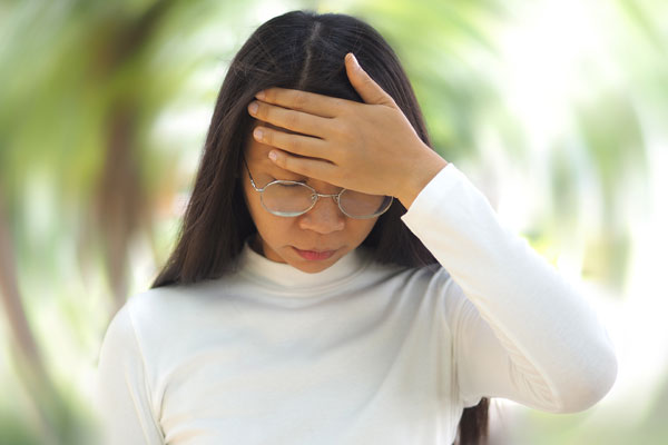 asian woman with glasses holding her head in dizziness